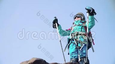 一个穿着鲜艳西装的登山者站在山顶上，<strong>举起双手</strong>，<strong>举起</strong>滑雪杆，高兴地站起来